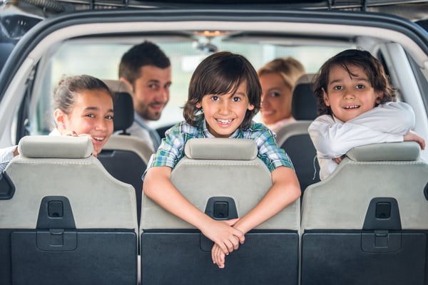 Playful kids posing in the back of a car with their parents in background